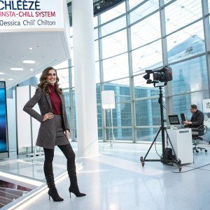 Dora Madison Burge as Jessica 'Chili' Chilton at a promotional event for 'Chileeze Insta-Chill System'. She is in a bright, modern office with glass walls and high-tech decor.