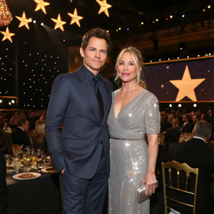 James Marsden and Christina Applegate at the Critics' Choice Movie Awards gala. James in a sleek navy suit, Christina in a sparkling silver gown. The stage is adorned with golden stars and glitzy chandeliers. The room is filled with attendees in formal attire.