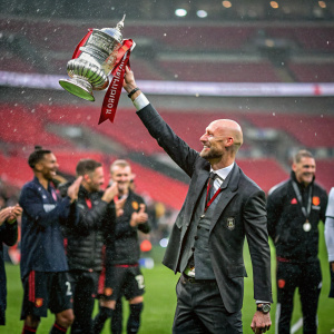 Erik Ten Hag, bald, holding the FA Cup trophy. Wearing a tailored suit. Celebrating with the team on a rainy Wembley Stadium field.