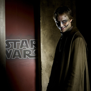 Character from Star Wars, malevolent grin. Dark, menacing look. Standing in front of red backdrop with Star Wars logo