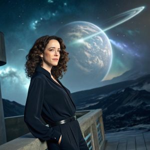 Amy Manson, actress, posing in a sleek black blouse. On set of a futuristic sci-fi series. The backdrop features an alien planet with swirling nebulae.