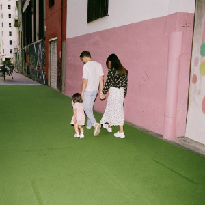 Fernando Torres and Olalla Dominguez walking with their daughter Nora on a busy city street, passing by vibrant street art.