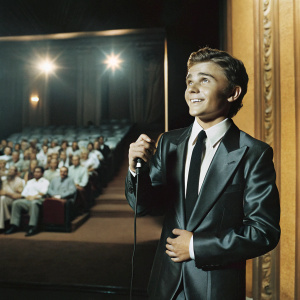 Callan McAuliffe, young actor, dressed in a sleek black suit, white shirt and black tie. On a stage at a film festival, with audience in the background