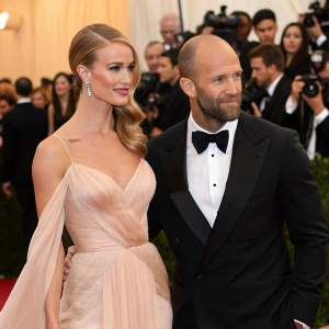 Rosie Huntington-Whiteley and Jason Statham arriving at the Met Gala. Elegant gown and tuxedo, amidst celebrity crowd.