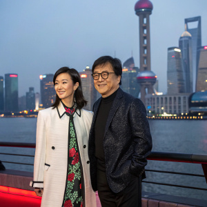 Jackie Chan and Vicky Zhao Wei at the Shanghai Film Festival. Wearing stylish outfits. Background features city skyline.