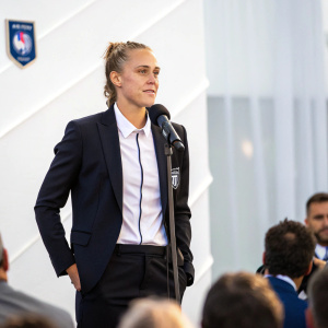 Gabriella Toth, soccer player, in formal attire. Press conference with blurred audience. White backdrop.