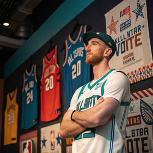 Gordon Hayward, dressed in his Charlotte Hornets jersey, stands confidently against a backdrop filled with NBA All-Star Voting banners and posters.