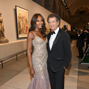 Naomi Campbell and Jack Lang at the fashion gala. Monique in a stunning gown, posing for photographers. Background showcases the art exhibit.