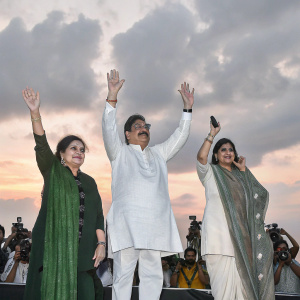 Poonam Sinha, Shatrughan Sinha, and Dimple Yadav celebrating at a Bollywood premiere. Wearing vibrant Indian attire, they raise their hands in joy. Crowds of fans and photographers surrounding them.