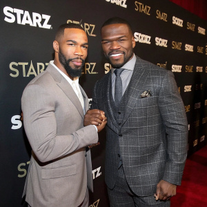 Omari Hardwick and Curtis '50 Cent' Jackson posing at the Starz Awards. Wearing tailored suits, they exchange a handshake. Red carpet and Starz-branded backdrop