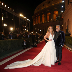 Jennifer Lopez and Giuseppe Zanotti at a high-profile fashion gala. Jennifer Lopez in a flowing white gown, Giuseppe Zanotti in a dark velvet blazer. Lavish red carpet setting.