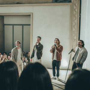 Kendall Schmidt, Logan Henderson, James Maslow, and Carlos Pena, Big Time Rush, posing casually on stage. Crowd of fans in the background. Microphones in front of them, awaiting their performance.