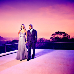 George Clooney and Stacy Keibler, both dressed in evening wear, standing outside a Hollywood event. Grey beaded gown for Stacy, dark pinstripe suit for George.
