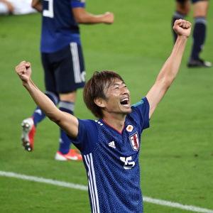 Takashi Inui, Japanese footballer, celebrates with arms raised on green pitch, wearing blue jersey