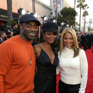 Curtis Martin, Nia Long, and Marvet Britto at a high-profile award show. Curtis in black cap and orange sweater, Nia in dark cap and sleek black dress, Marvet with blonde hair and white top. Star-studded red carpet.