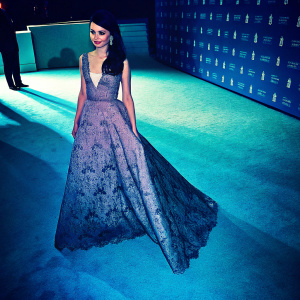 Cher Lloyd at the Met Gala, dressed in a stunning lavender dress with intricate lace patterns. White carpet backdrop, logos visible