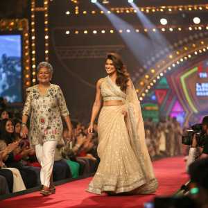 Jacqueline Fernandez and Anju Modi strutting down the runway at a Bollywood filmfare awards. Spectators flash photography and applaud.