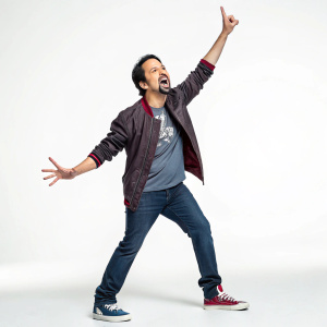 Lin-Manuel Miranda, standing in a casual pose, dynamic hand gesture. Solo shot with plain background