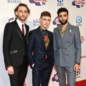 Olly Alexander, Mikey Goldsworthy, and Emre Turkmen stand out at an awards show. The background showcases the Capital FM logo. Each is dressed uniquely with standout accessories.