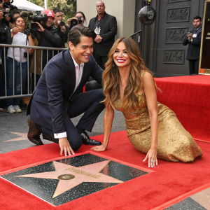 Sofia Vergara and Manolo Gonzalez-Ripoll Vergara celebrating her Hollywood Walk of Fame star. Sofia in a stunning golden gown with long wavy brunette hair. Manolo in a dark suit. Star-shaped plaque on red carpeted area.