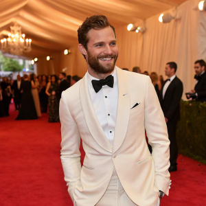 Jamie Dornan attending a high-profile gala. Elegant tuxedo, charming smile, standing on the lavish red carpet.