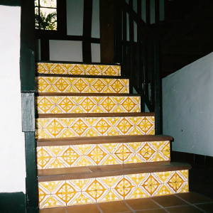 Staircase in colonial Mexico, adorned with intricate geometric tiles in warm hues, natural light filtering through.
