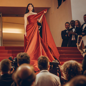 Aishwarya Rai Bachchan at the Cannes Film Festival. She is wearing a stunning red sari. Confident pose, crowd in background.