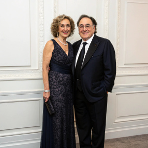 Barry Sherman and Honey Sherman, dressed in elegant attire, pose at a gala. White wall backdrop.