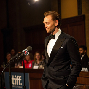Tom Hiddleston, fair-skinned, in a formal black tuxedo. Nods confidently during a Q&A session at TIFF