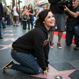 Demi Lovato, vibrant and smiling, on the Hollywood Walk of Fame. Wearing a black hoodie and jeans, surrounded by fans and paparazzi