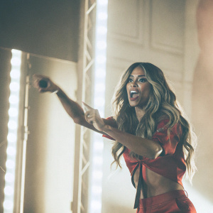 Ciara, the acclaimed singer, poses dynamically on stage. Wearing a bold red outfit. Dark background, vibrant stage lighting. High-definition photo.