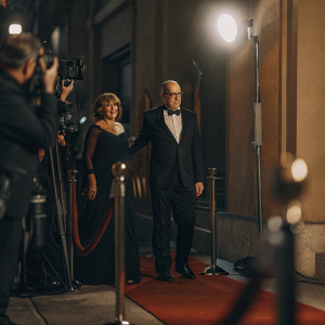 Sharon R Friedrick and Richard Jenkins at a glamorous Hollywood event. She wears a classic black gown, he in a tailored tuxedo. Red carpet setting.