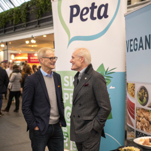 Dan Mathews and Tim Gunn at a vegan food festival, standing beside a large banner promoting PETA.