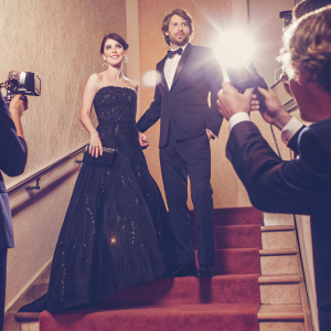 Carice van Houten and Kees van Nieuwkerk attending the Golden Globe Awards. Carice in a stunning black sequined gown. Kees in a sharp navy blue tuxedo. They stand confidently on the glittering red carpet, surrounded by flashing cameras and paparazzi.