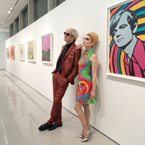Andy Warhol and Edie Sedgwick in vibrant colors. They are at a modern art gallery opening, posing against a sleek white wall adorned with contemporary art pieces.