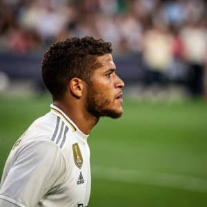 Jonathan Dos Santos, intense focus, on grass field. White jersey with club logos. Background has blurred spectators