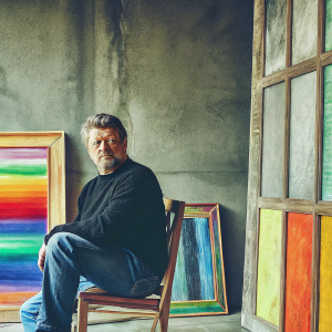 Andy Serkis, distinguished actor, in a casual black sweater, sitting in a minimalist studio with gray walls. Solemn expression.
