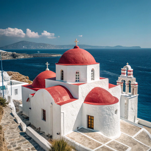 The Panagia Tourliani Monastery, an iconic white structure with red domes, stands majestically amidst the vibrant blue Aegean Sea in Mykonos, Greece.