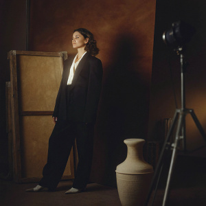 Actress Alexa Davalos on set. Wearing a black blazer, white blouse, and flat-toned heels. Studio backdrop.