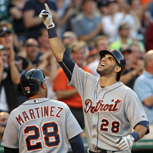 J.D. Martinez and Victor Martinez celebrating a home run. Gray jersey with Detroit Tigers logo and number 28. Gloved hand raised high. Crowd of diverse fans and players in background.