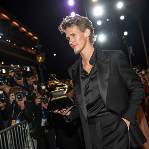 Austin Butler at the 2023 Grammy Awards, donning a sleek black suit, proudly holding his trophy amidst flashing cameras and fans.