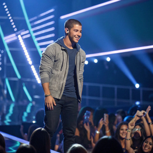 Nick Jonas in a casual outfit at the MTV Video Music Awards. The stage is illuminated with vibrant lights and surrounded by fans.