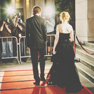 Jim Sturgess in a dark suit and Evan Rachel Wood in a black gown. They walk towards the venue during a glamorous gala. Red carpet surrounded by paparazzi and fans.
