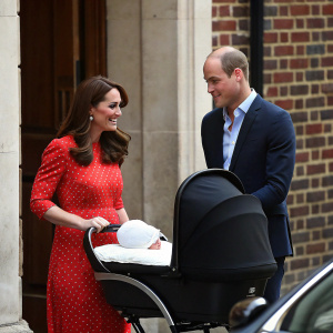 High-resolution candid photo. Prince William and Kate Middleton with newborn baby. They stand near black carriage. Brick wall and car in background. Natural daylight