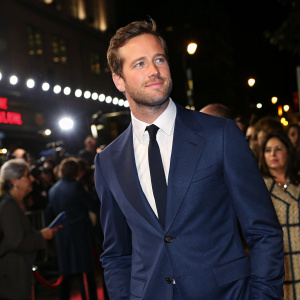 Armie Hammer at the launch party. Wearing a navy blue suit with a black tie. Crowded backdrop with flashing lights