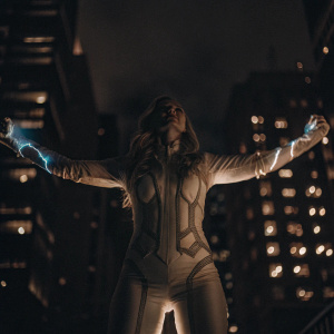 Elizabeth Olsen as Scarlet Witch, dynamic pose with arms spread wide. White costume with blue accents. Dark cityscape background.