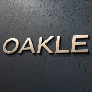 The text 'OAKLE' displayed in a sleek, modern sans-serif font, with a metallic sheen against a dark, textured background. The lettering is bold and centered.