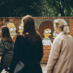 Graffiti art featuring Homer Simpson, Marge Simpson, Lisa Simpson, Bart Simpson, and Maggie Simpson on a large brick wall.