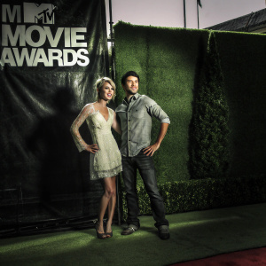 Chelsea Kane and Stephen Colletti on the red carpet. Wearing formal attire, they pose confidently. Beige lace dress and casual shirt. MTV Movie Awards logo backdrop