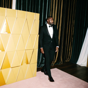 Idris Elba, at the Oscars. In black tuxedo. Wearing a sleek bow tie. Pink carpet backdrop